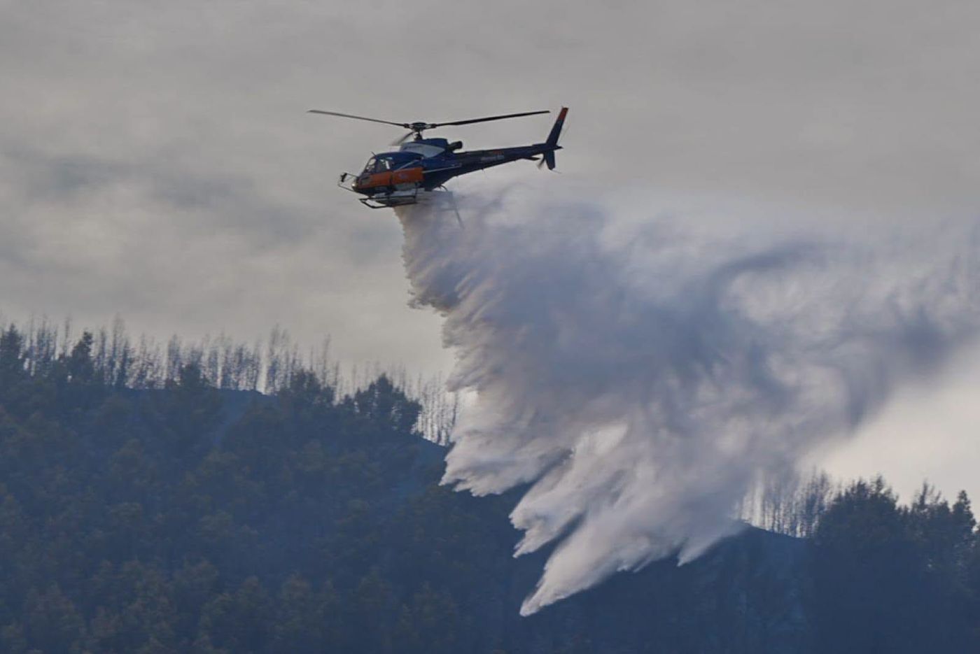 Een blushelikopter dropt een lading bluswater boven een bebost gebied tijdens de bosbrand in de Var.